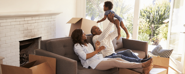 black man and woman holding baby in air above couch