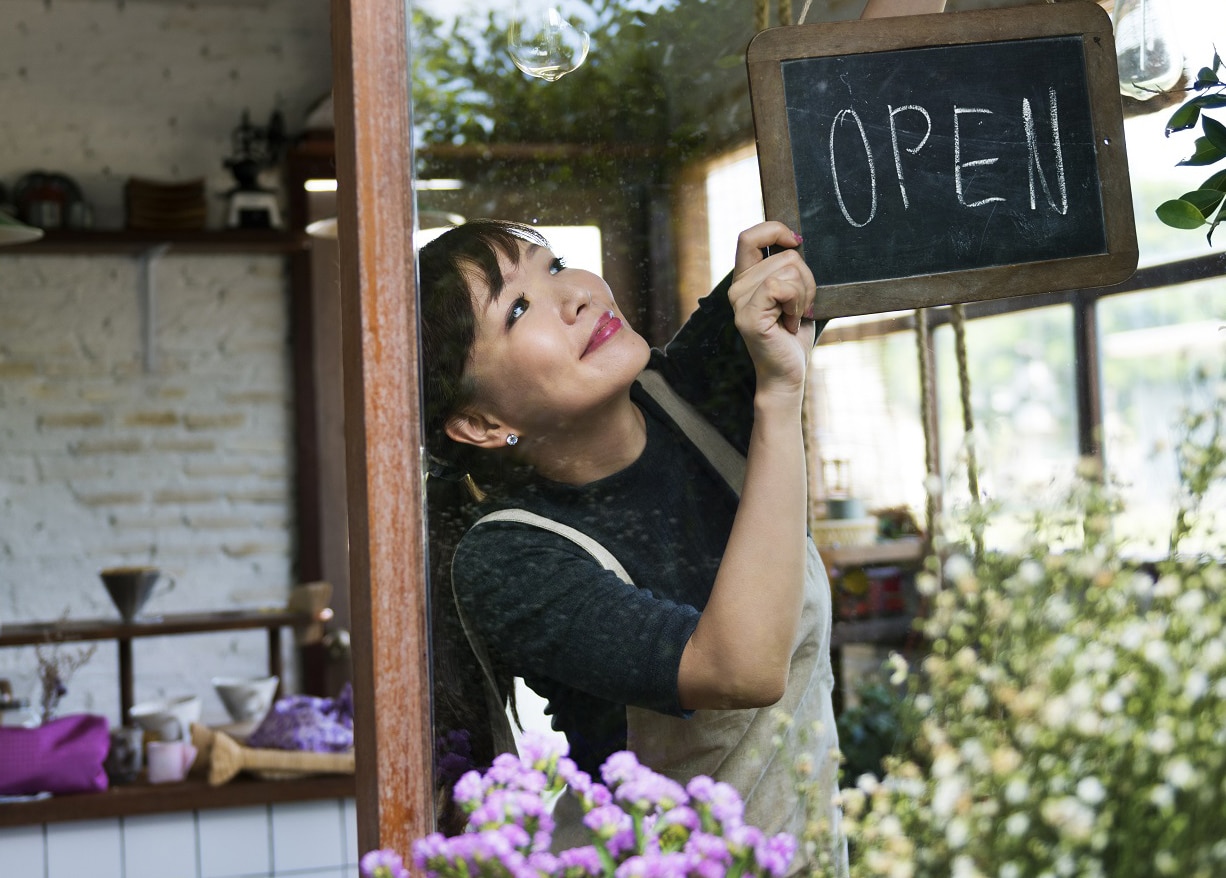 asian woman hanging Open sign in flower store window