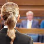 back of white female attorney who is facing courtroom audience